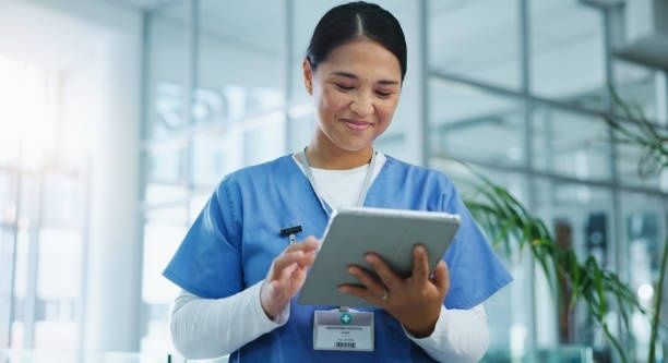 Sundhedsansat i blå uniform bruger en tablet på hospitalet